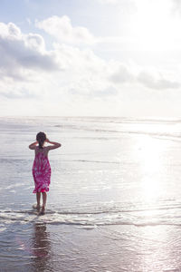 Rear view of girl standing on beach against sky during sunny day