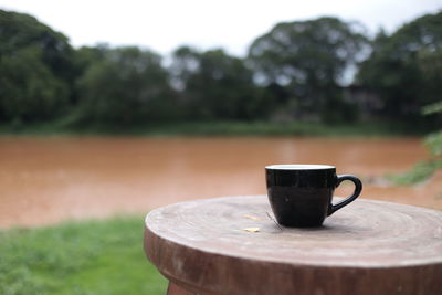Close-up of coffee cup on wood by the river