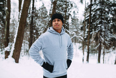 Young man wearing warm clothing while standing against trees during winter