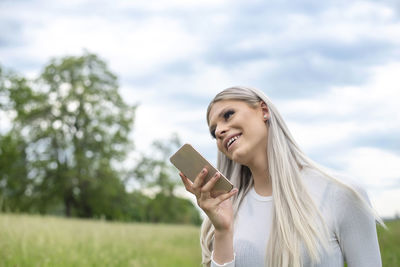 Portrait of smiling young woman using smart phone against sky