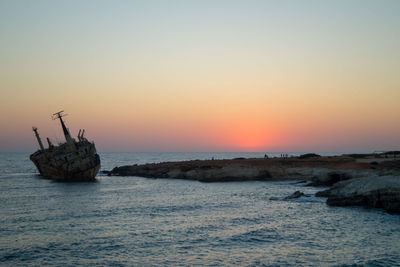 Sailboat on rock in sea against sky during sunset