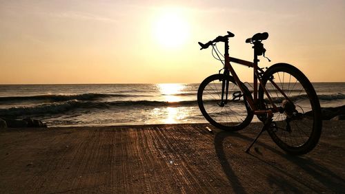 Silhouette bicycle on beach against sky during sunset