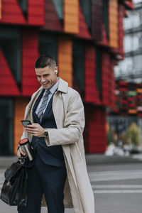 Happy businessman using smart phone while standing at street