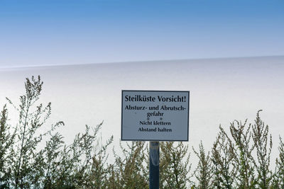 Information sign board by trees against clear sky