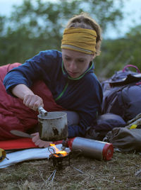 Female hiker making drink while leaning on bed at field during camping