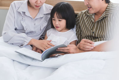 High angle view of friends reading book on bed