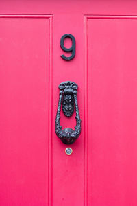 House number 9 on a bright pink wooden front door with door knocker 