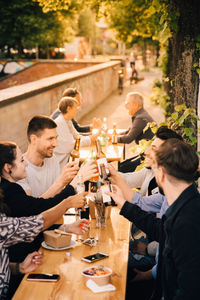 Happy male and female friends toasting beer while sitting in garden