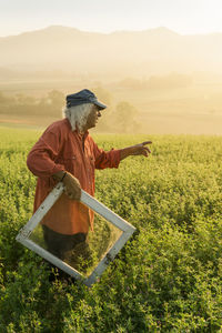 Italy, tuscany, borgo san lorenzo, senior man holding window frame in field at sunrise