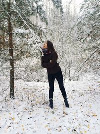 Full length of woman licking snow covered tree in forest