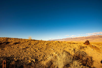 Scenic view of arid landscape against clear blue sky with distant snowy mountains