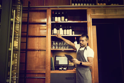 Male owner checking list of wine bottles while standing in cafe