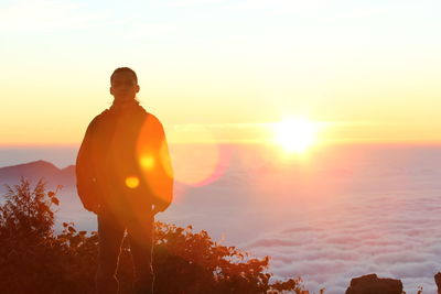 Silhouette man standing against bright sun during sunset