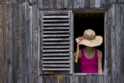 Rear view of woman wearing hat on wooden window