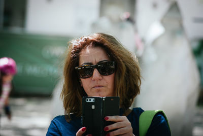 Portrait of woman photographing with mobile phone while standing outdoors