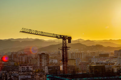 Cranes at construction site against sky during sunset