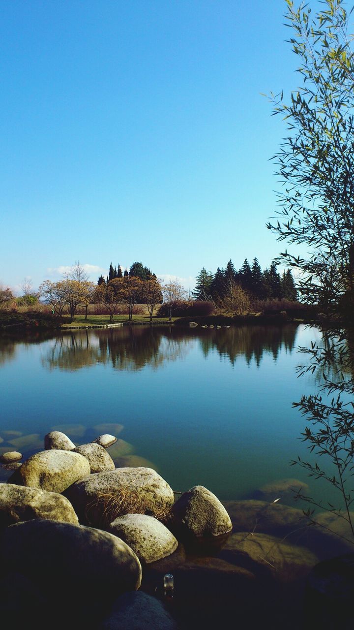 clear sky, water, reflection, tranquility, blue, tranquil scene, copy space, lake, tree, scenics, rock - object, beauty in nature, nature, standing water, river, stone - object, sky, idyllic, calm, outdoors