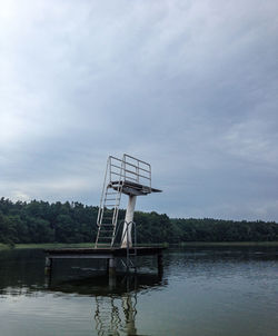 Diving platform over lake by trees against sky