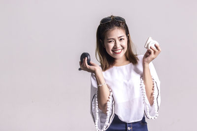 Portrait of woman holding make-up while standing against white background