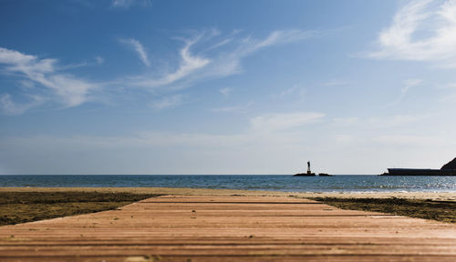 Wooden pathway on the beach with blue ocean and a lighthouse behind