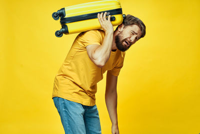 Side view of young man standing against yellow background