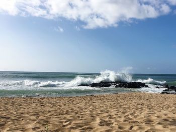 Waves splashing on rocks in sea against sky