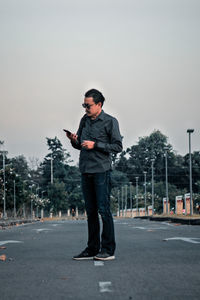 Full length of man using mobile phone while standing on road against sky