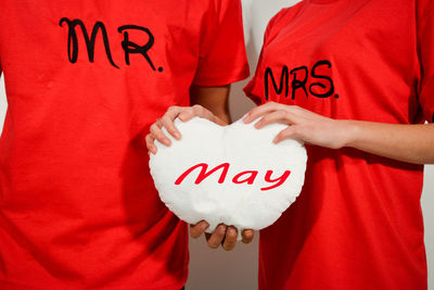 Midsection of couple holding heart shape with may text