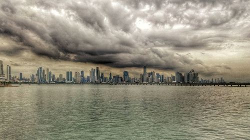 City at waterfront against cloudy sky