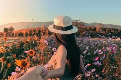 Cropped image of man holding woman by flowers on field 