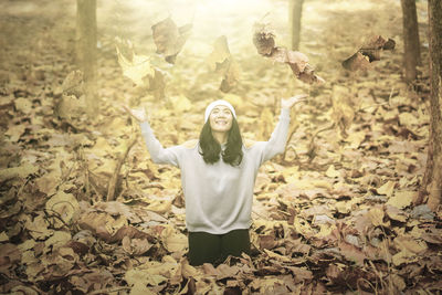 Portrait of young woman with arms outstretched standing on leaves