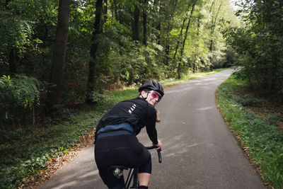 Rear view of man riding bicycle on road amidst trees