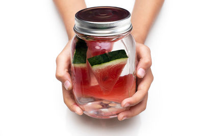 Close-up of hand holding glass jar against white background