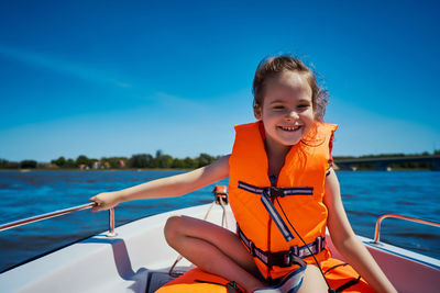 Happy girl sitting in boat on lake against blue sky