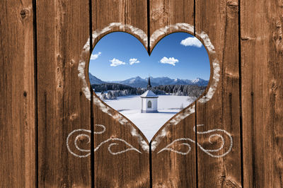 Looking through a carved heart in a wooden wall to a romantic chapel in winter