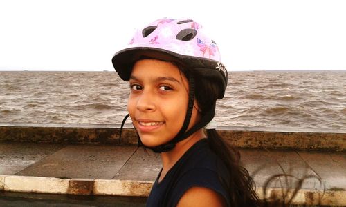 Portrait of smiling young woman standing at beach against clear sky