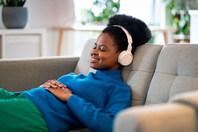 Calm african american woman listening to music in wireless headphones lying with closed eyes