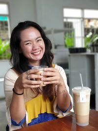 Portrait of smiling young woman holding coffee while sitting in cafe