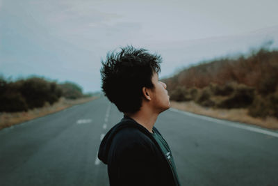 Portrait of young man standing on road against sky