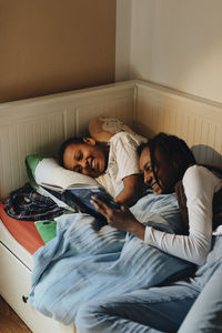 High angle view of brother and sister enjoying while reading story book on bed at home