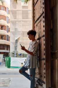 Young afro leaning on a wooden gate looking at his phone