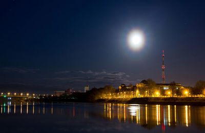 Illuminated city by river against sky at night