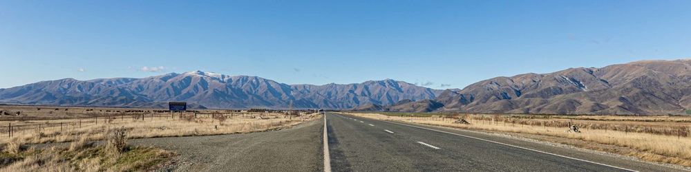 Road leading towards mountains against clear blue sky