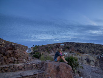 Woman on rock by mountain against sky