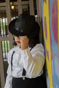 Portrait of girl wearing hat standing against wall