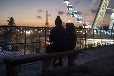 Rear view of couple sitting on bench at amusement park