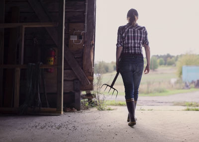 Rear view of female farmer with pitchfork walking in barn