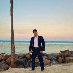 Young man standing on rocks by sea against sky