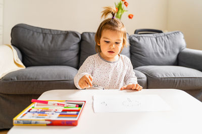 Girl with felt tip pens drawing at table in living room