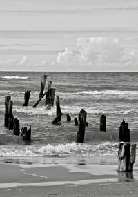 Wooden pillars in sea against cloudy sky